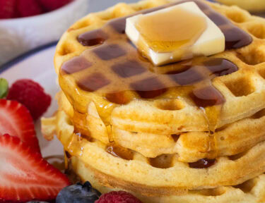 Easy homemade waffles stacked on a plate with butter and syrup. Fresh berries on the side.