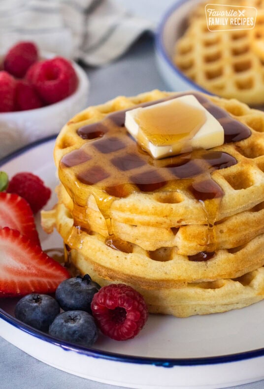 Easy homemade waffles stacked on a plate with butter and syrup. Fresh berries on the side.