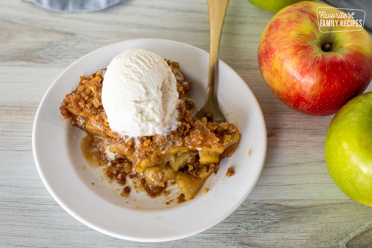 Gluten Free Apple Pie on a plate with a fork cutting into it. Vanilla ice cream on top and melted a little into the pie.