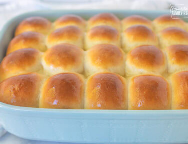 Baking dish of baked homemade dinner rolls with melted butter brushed on top.