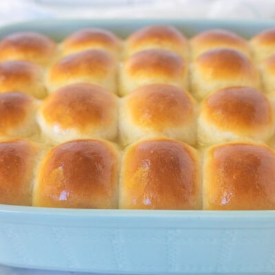 Baking dish of baked homemade dinner rolls with melted butter brushed on top.