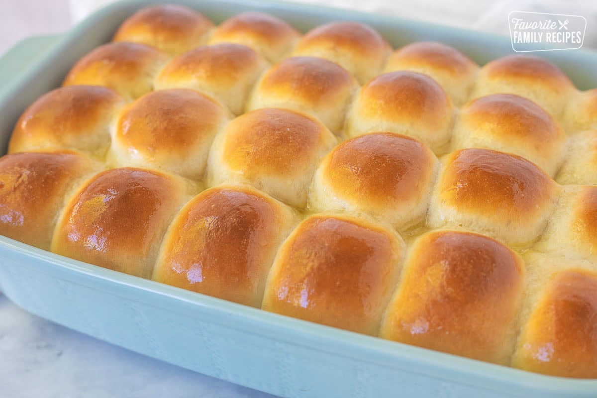 Baking dish of baked homemade dinner rolls with melted butter brushed on top.