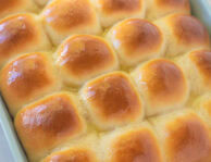 Baking dish of baked homemade dinner rolls with melted butter brushed on top.