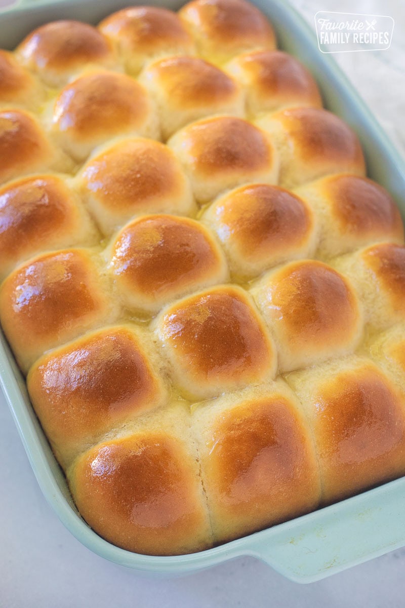 Baking dish of baked homemade dinner rolls with melted butter brushed on top.