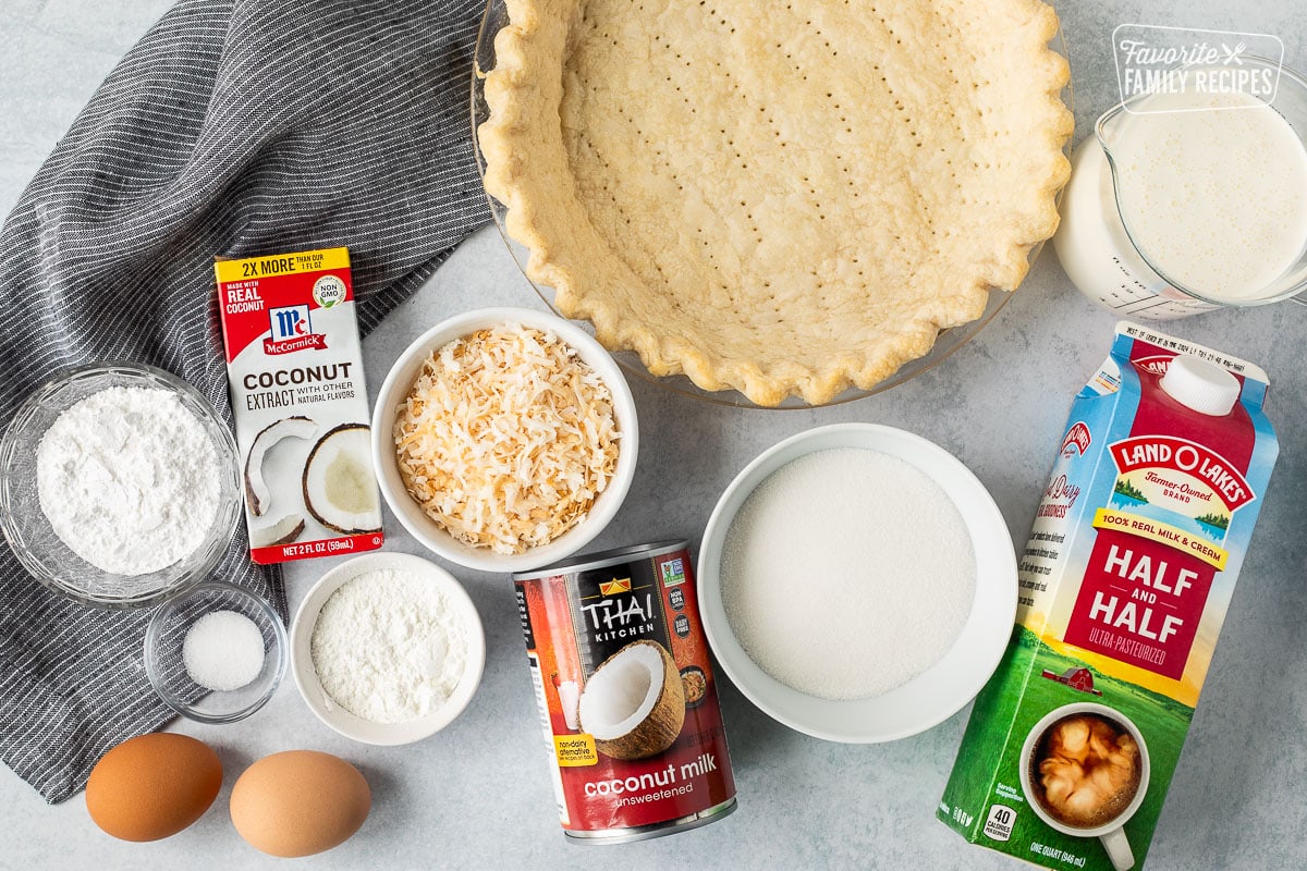 Ingredients to make Coconut Cream Pie including a pie crush, half and half, whipping cream, sugar, toasted coconut, coconut milk, corn starch, salt, eggs, coconut extract and flour.