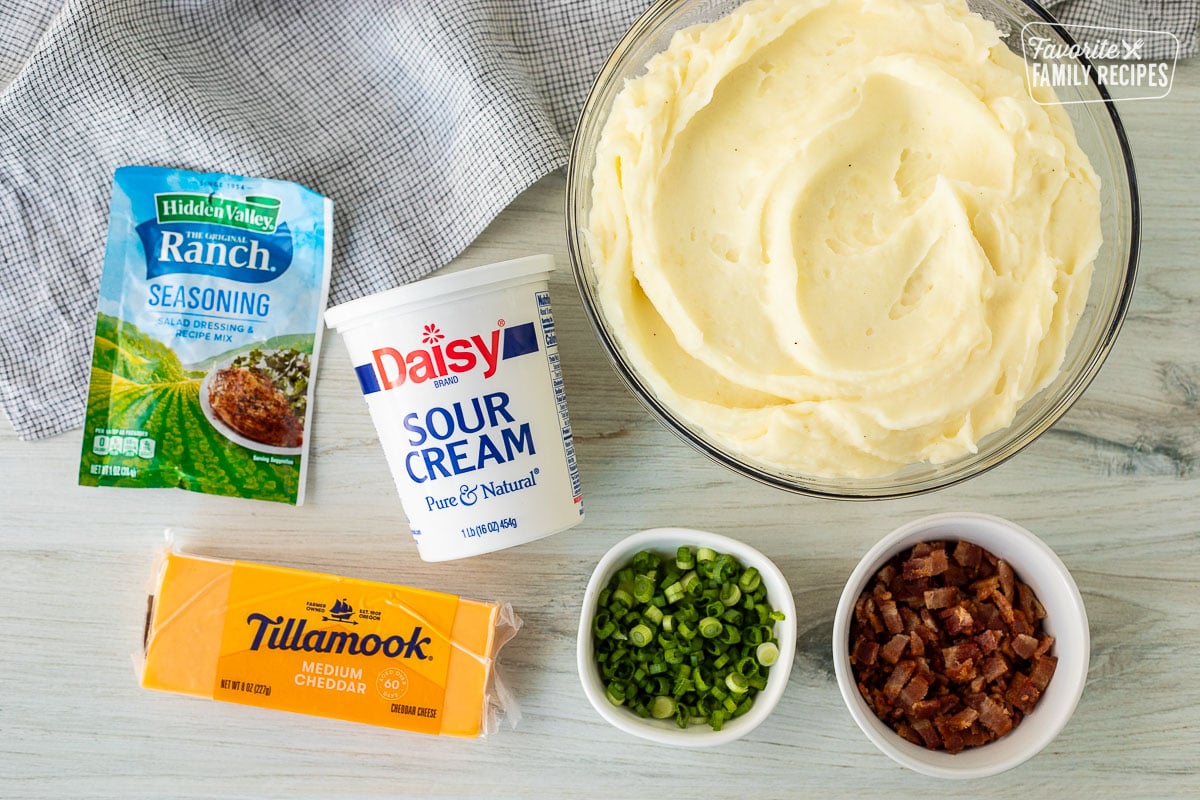 Ingredients for Loaded Mashed Potatoes including mashed potatoes, sour cream, ranch dressing seasoning, cheddar cheese, green onions and bacon.