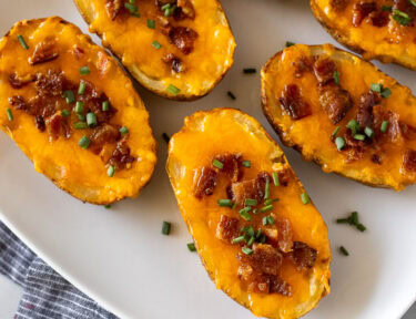 Loaded potato skins with melted cheese, bacon, and chives on a platter.