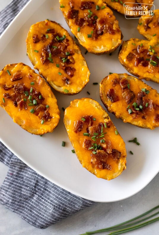 Loaded potato skins with melted cheese, bacon, and chives on a platter.