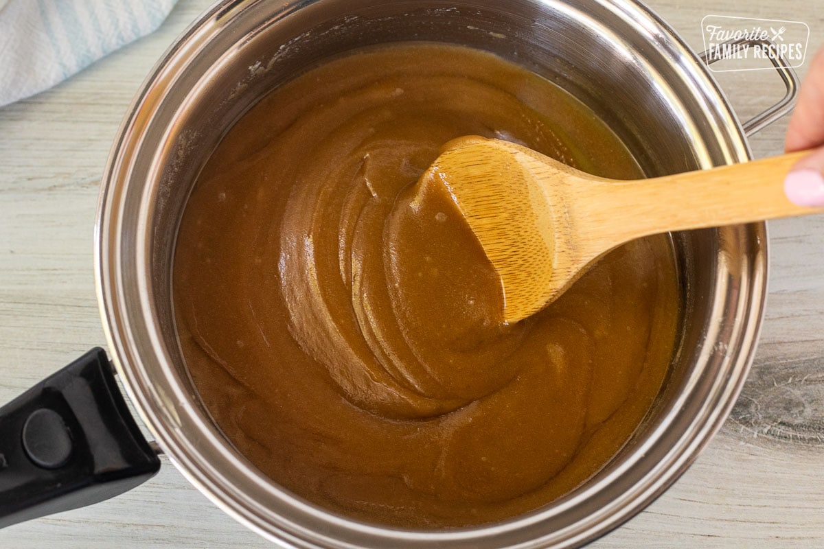 Saucepan with brown sugar butter mixture and a wooden spoon stirring.