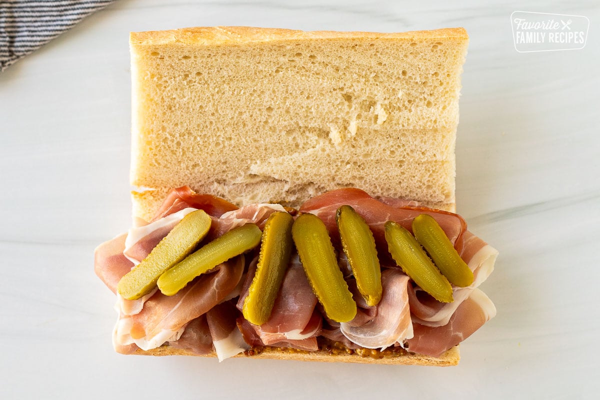 Small baby pickles on top of prosciutto in a raclette sandwich.