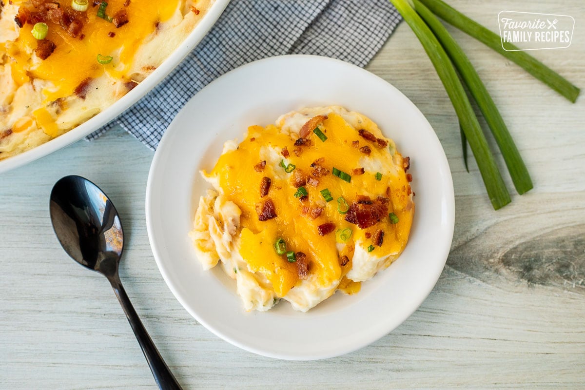 Plate with a serving of Loaded Mashed Potatoes garnished with bacon and green onions.