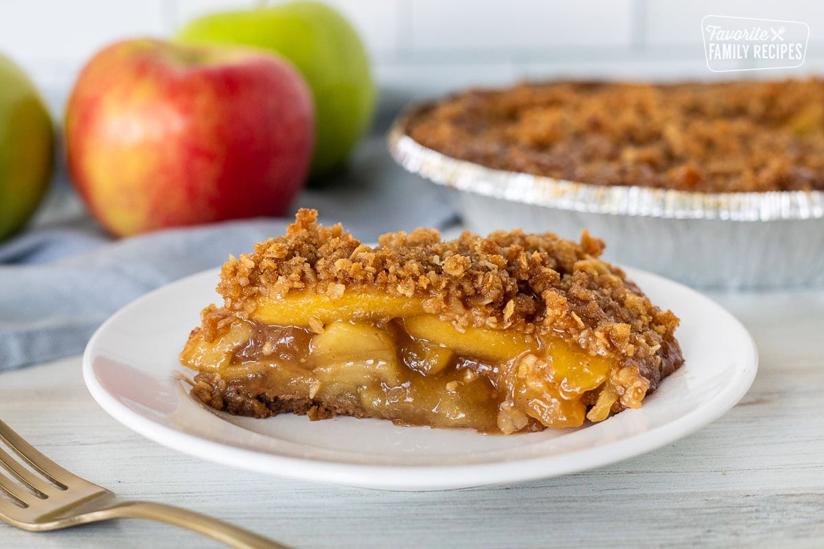 Slice of Gluten Free Apple Pie on a plate. Fork on the side and whole pie in the background.