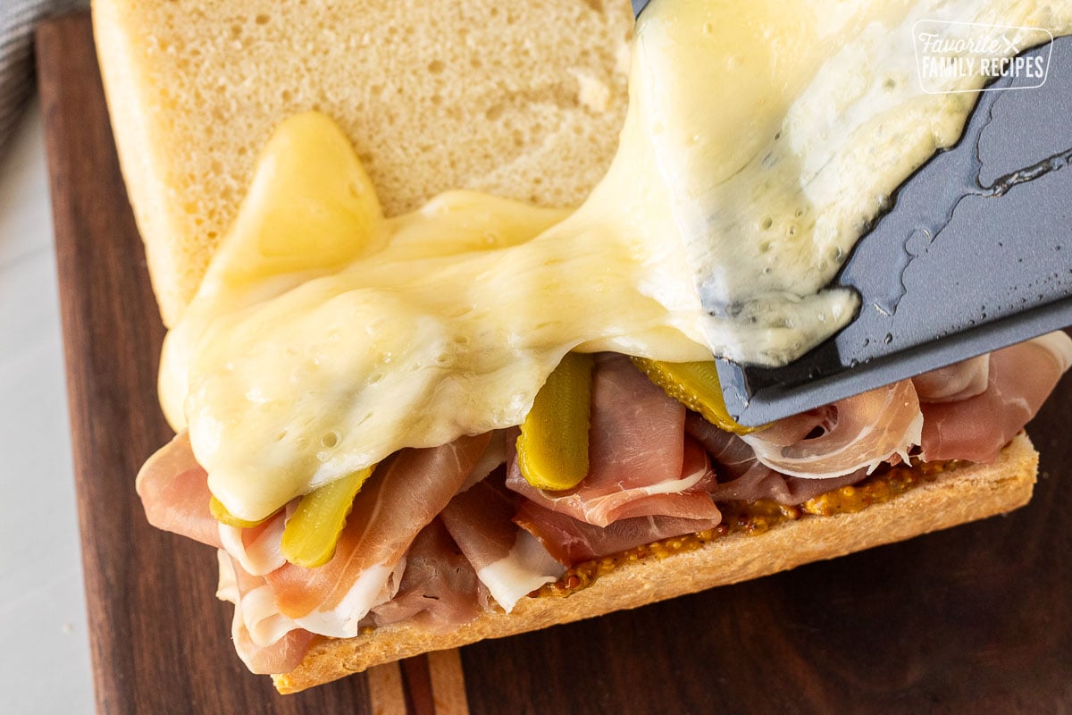 Pouring melty raclette cheese on top of a sandwich.