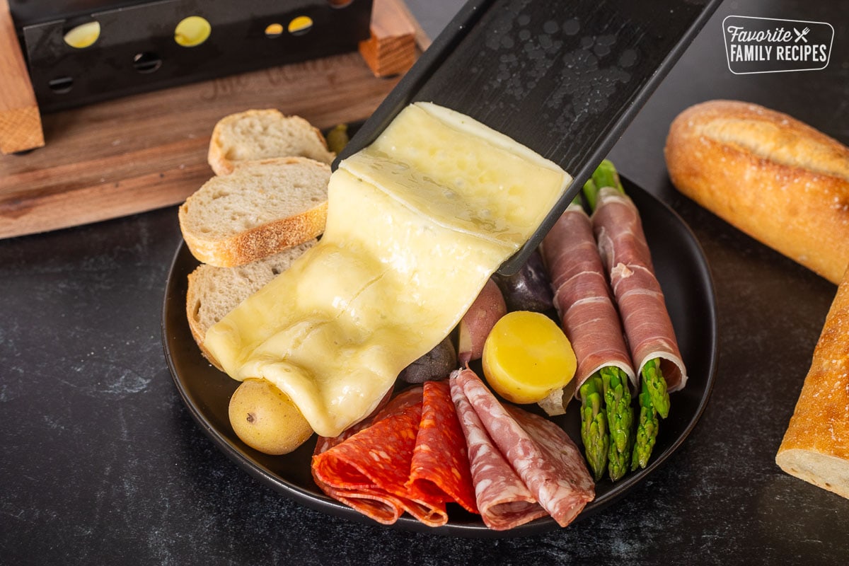 Pouring Raclette onto plate with meat, potatoes, bread and asparagus.