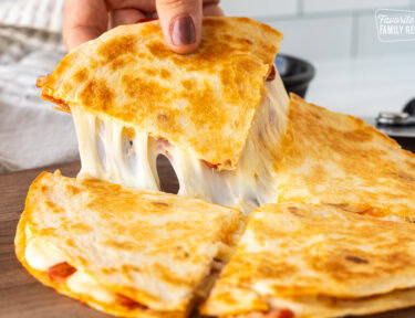 Hand picking up a slice of cheesy pizza quesadilla.