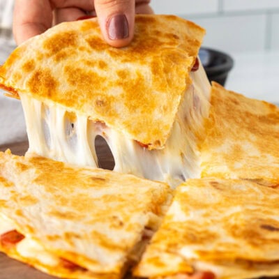 Hand picking up a slice of cheesy pizza quesadilla.