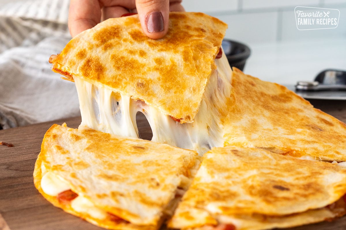 Hand picking up a slice of cheesy pizza quesadilla.