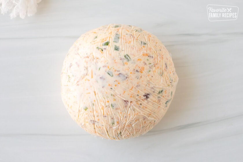 Round shaped cheese ball wrapped in plastic wrap.