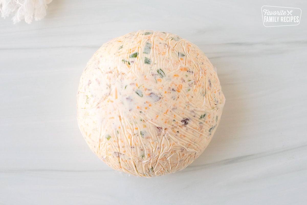 Round shaped cheese ball wrapped in plastic wrap.