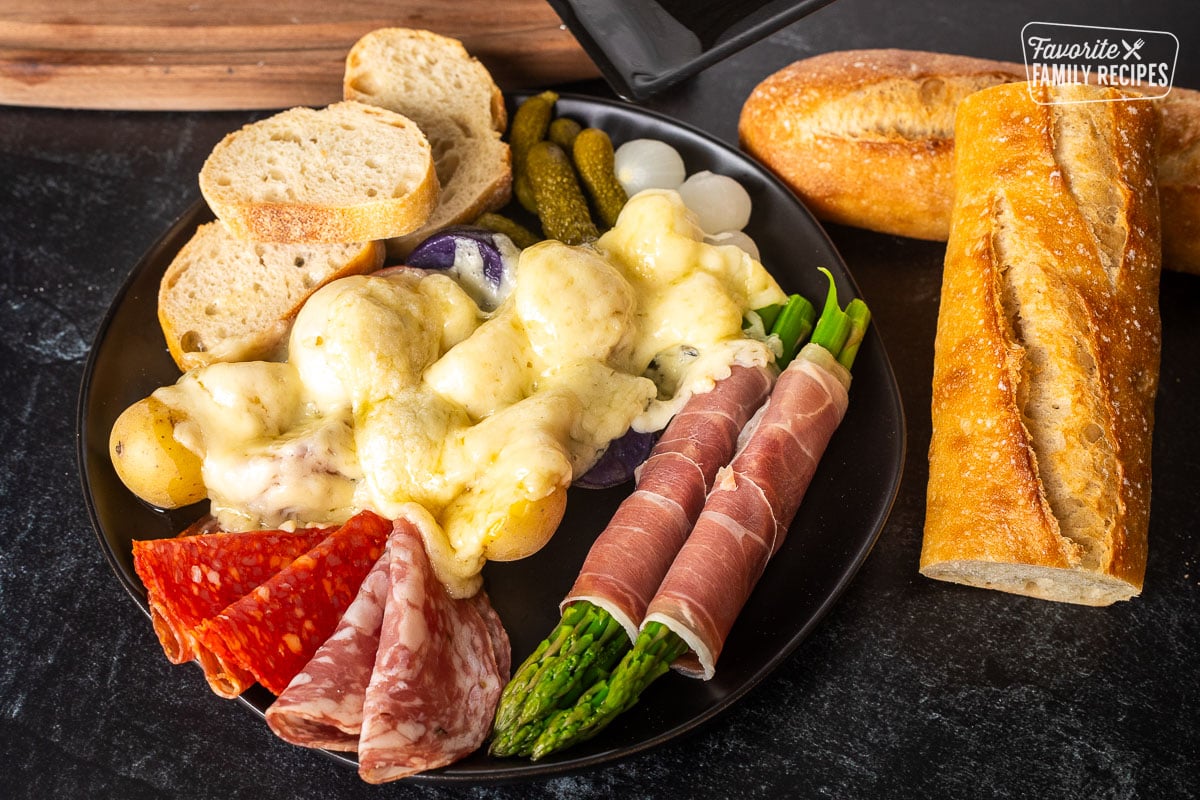 Raclette on a plate with meat, potatoes, bread and asparagus.