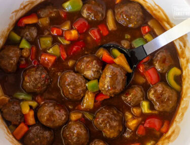 Spooning in a Crock pot of sweet and sour meatballs.