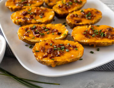 Side of loaded potato skins on a platter with melted cheddar cheese, crispy bacon, and chives.