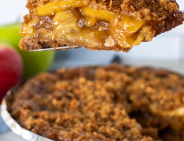 Slice of Gluten Free Apple Pie held up with a pie server. Whole pie in the background.