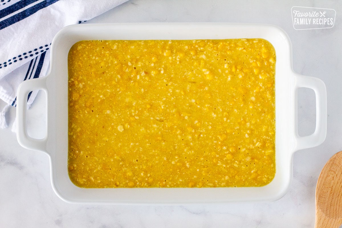 Corn Casserole mixture in a baking dish next to a wooden spoon.