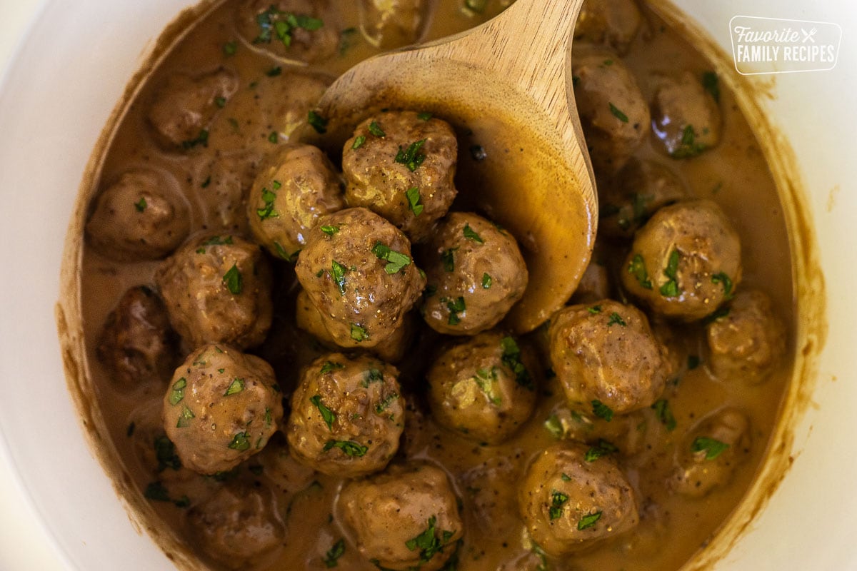 Spoon holding a scoop of Swedish Meatballs in a crock pot.