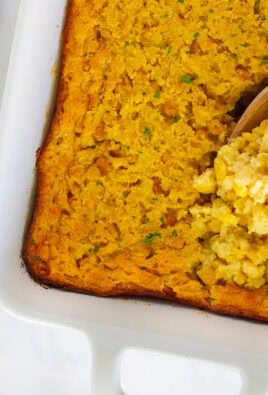 Wooden spoon with scooped corn casserole in a baking dish.