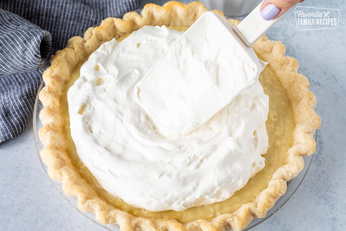 Spreading whipped topping on a Coconut Cream Pie with a spatula.