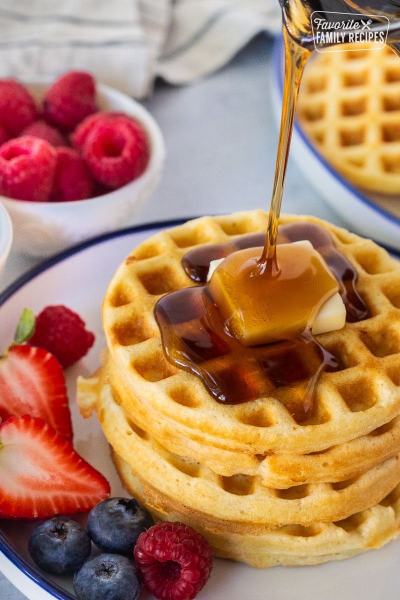 Pouring syrup onto a stack of waffles with a pad of butter.