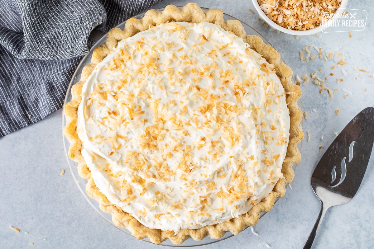 Whole Coconut Cream Pie with spatula and extra toasted coconut.