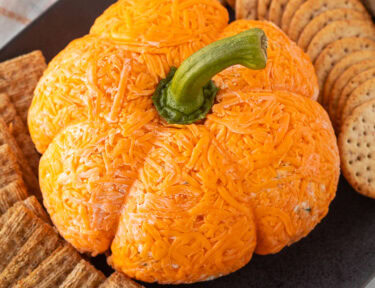 Pumpkin shaped cheese ball on a platter with crackers.