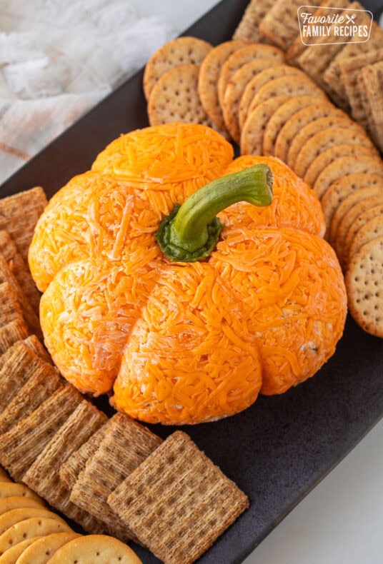 Pumpkin shaped cheese ball on a platter with crackers.