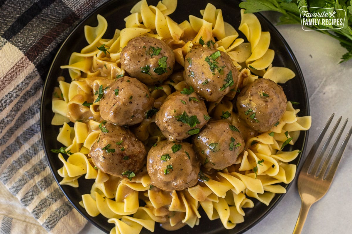 Crock Pot Swedish Meatballs over noodles on a plate garnished with parsley.