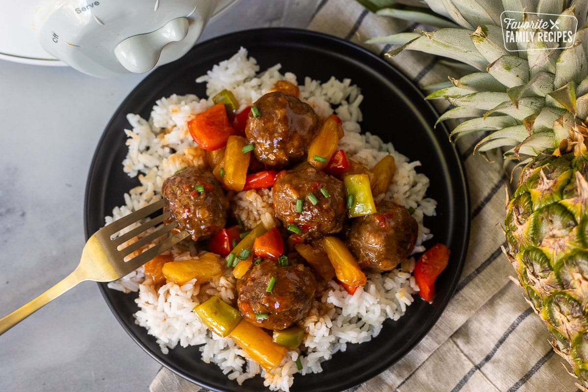 Plate of Crock pot of sweet and sour meatballs over rice. Fork is stabbing into a meatball.