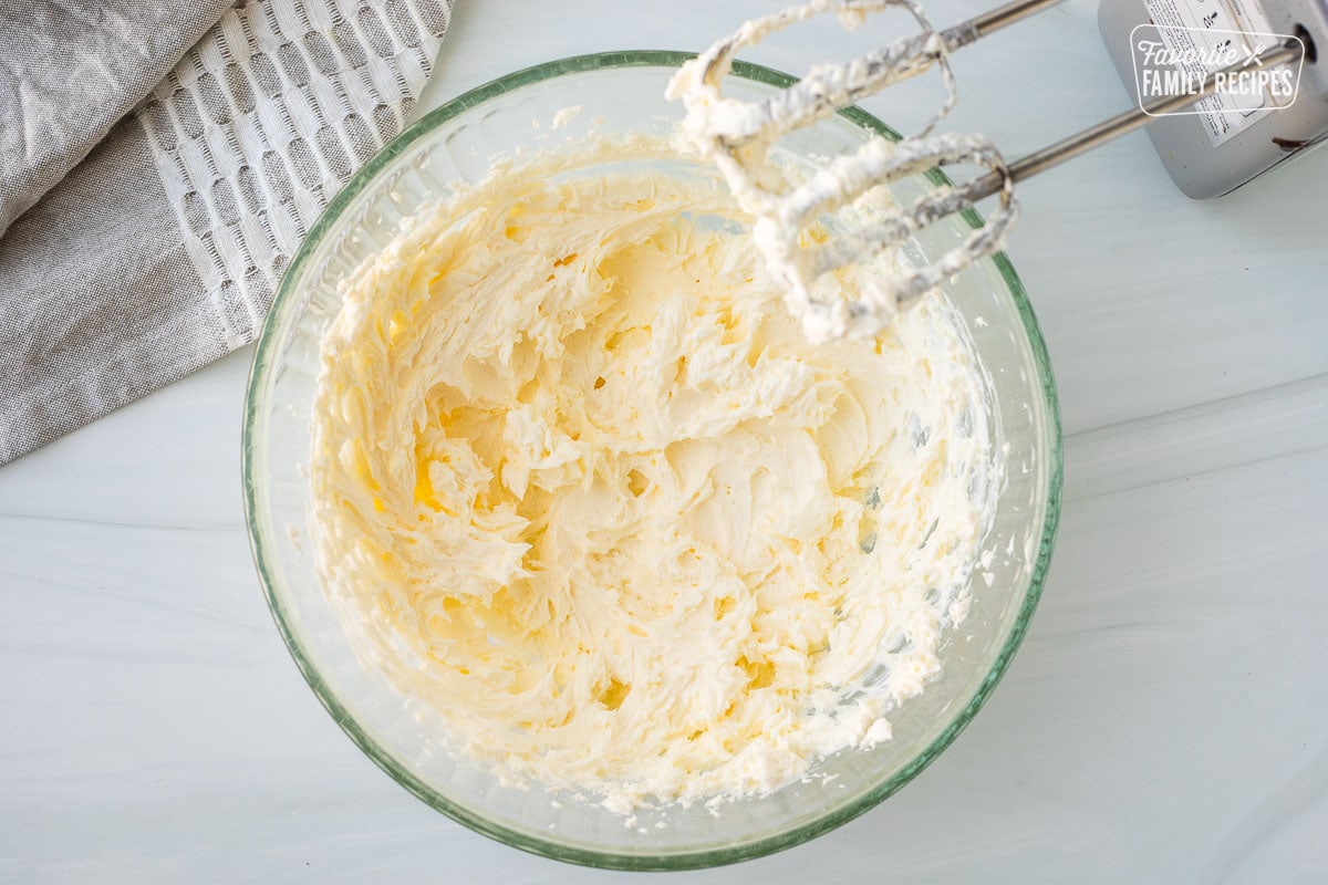 Mixing bowl with butter and cream cheese combined with an electric mixer.