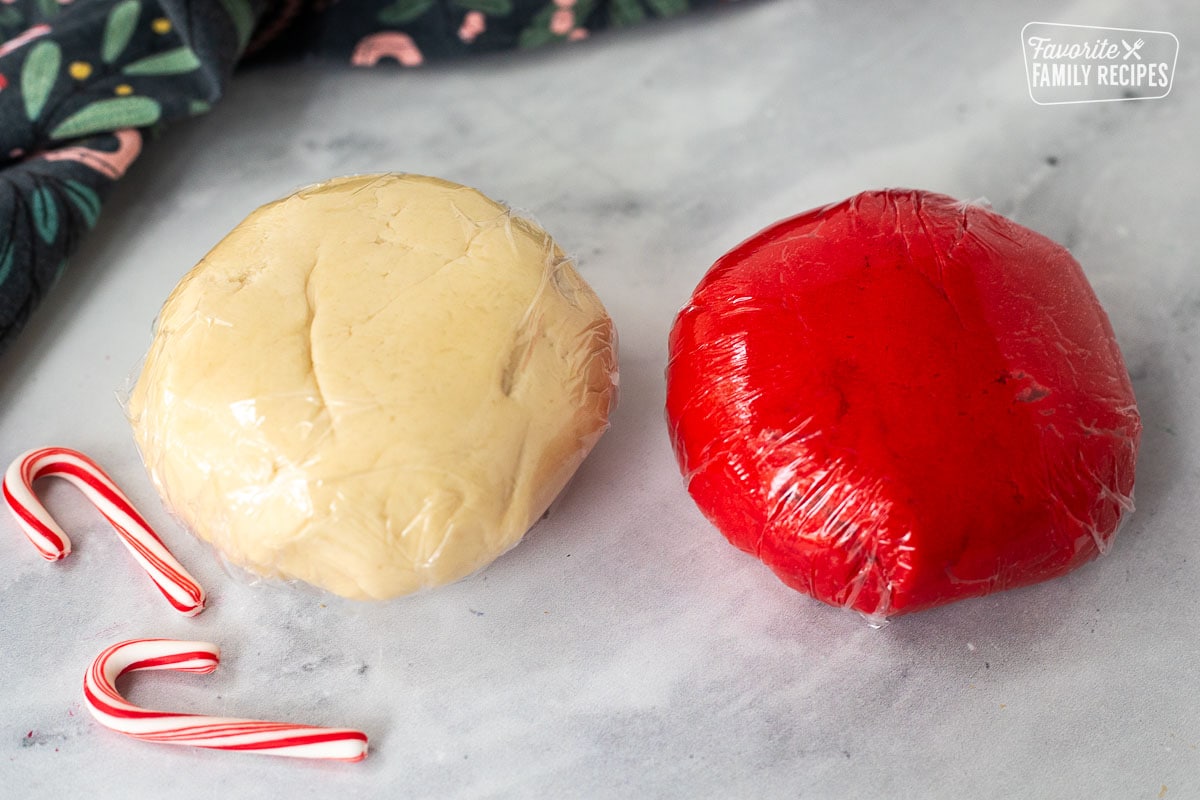 Two balls of cookie dough wrapped in plastic wrap. One is red one is white.