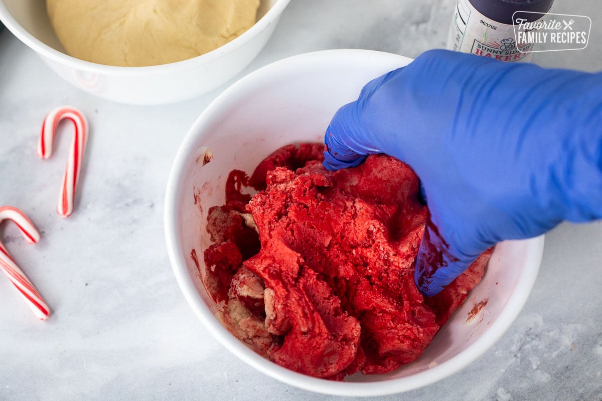 Gloved hand mixing red gel coloring into cookie dough.