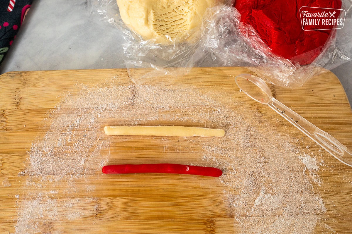 Floured board with rolled snake like shaped pieces of red and white candy cane cookie dough.