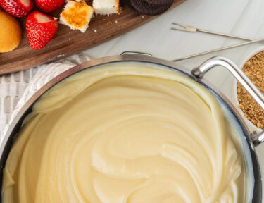 Cheesecake Fondue next to cutting board of cookies, cake and strawberries.