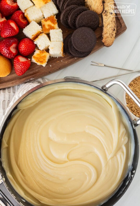 Cheesecake Fondue next to cutting board of cookies, cake and strawberries.