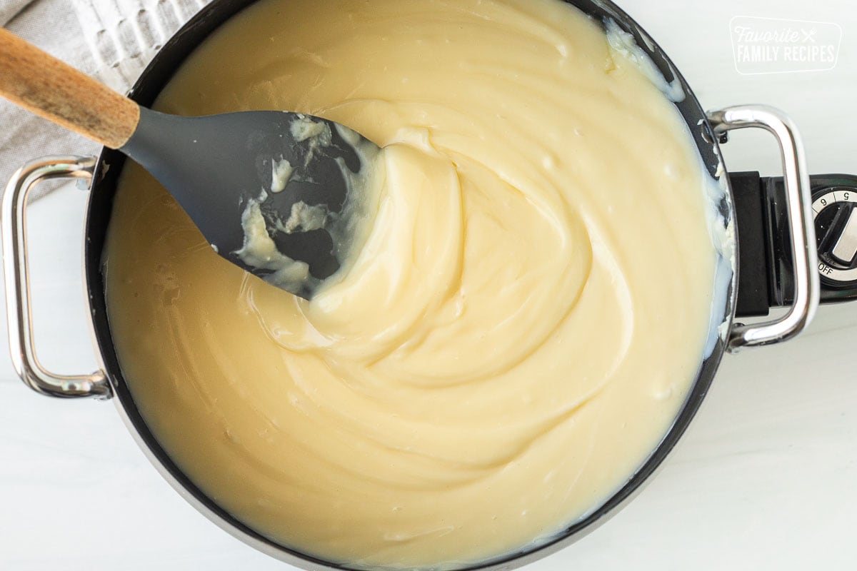 Stirring cheesecake fondue with spatula in fondue pot.