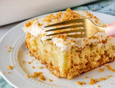 Slice of cinnamon roll cake on a plate with a fork cutting into slice.