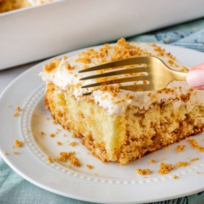 Slice of cinnamon roll cake on a plate with a fork cutting into slice.