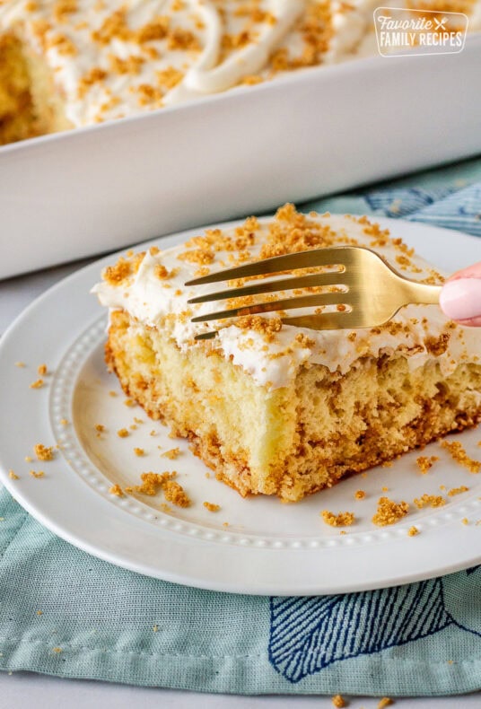 Slice of cinnamon roll cake on a plate with a fork cutting into slice.