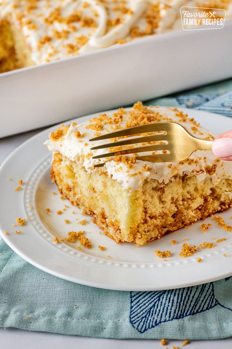 Slice of cinnamon roll cake on a plate with a fork cutting into slice.