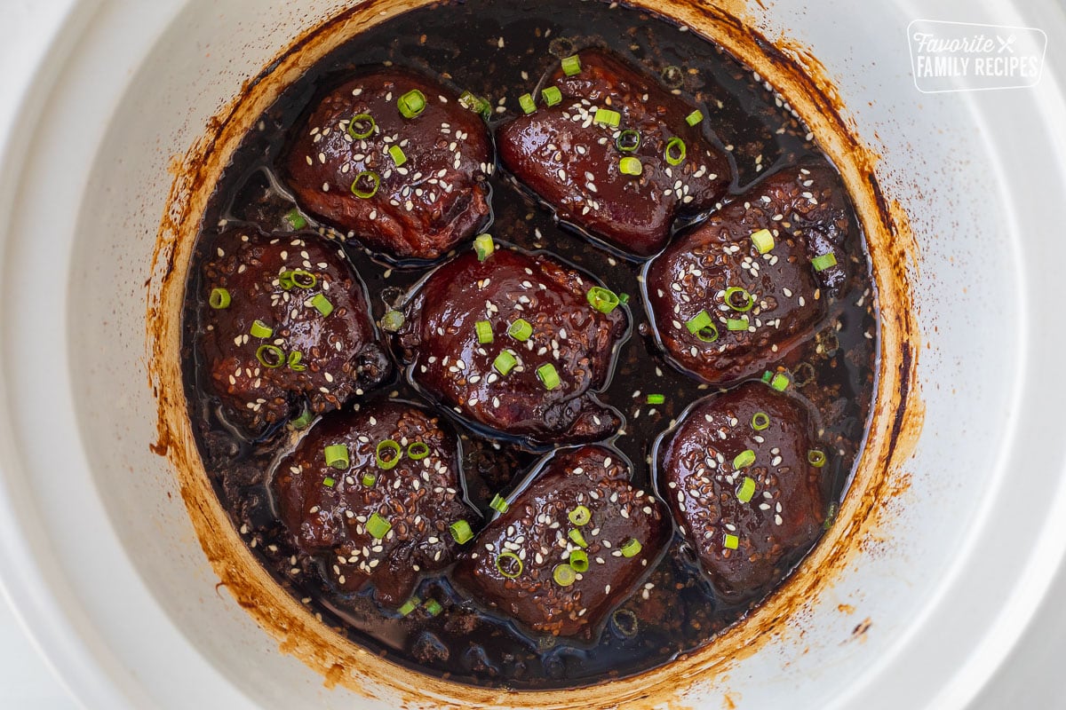 Crockpot with cooked Hawaiian chicken thighs, garnished with green onion and sesame seeds.