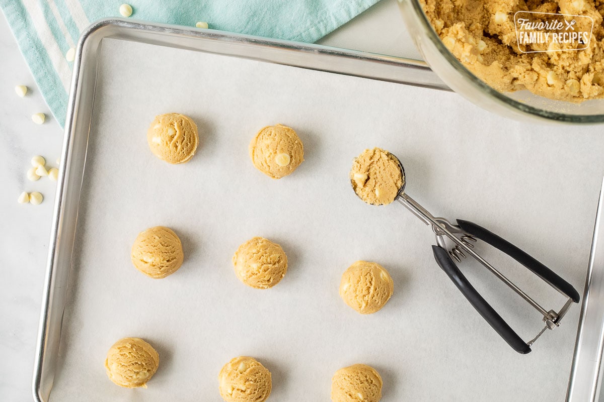 Baking sheet with parchment paper and scoops of White Chocolate Chip cookie dough with a cookie scoop.